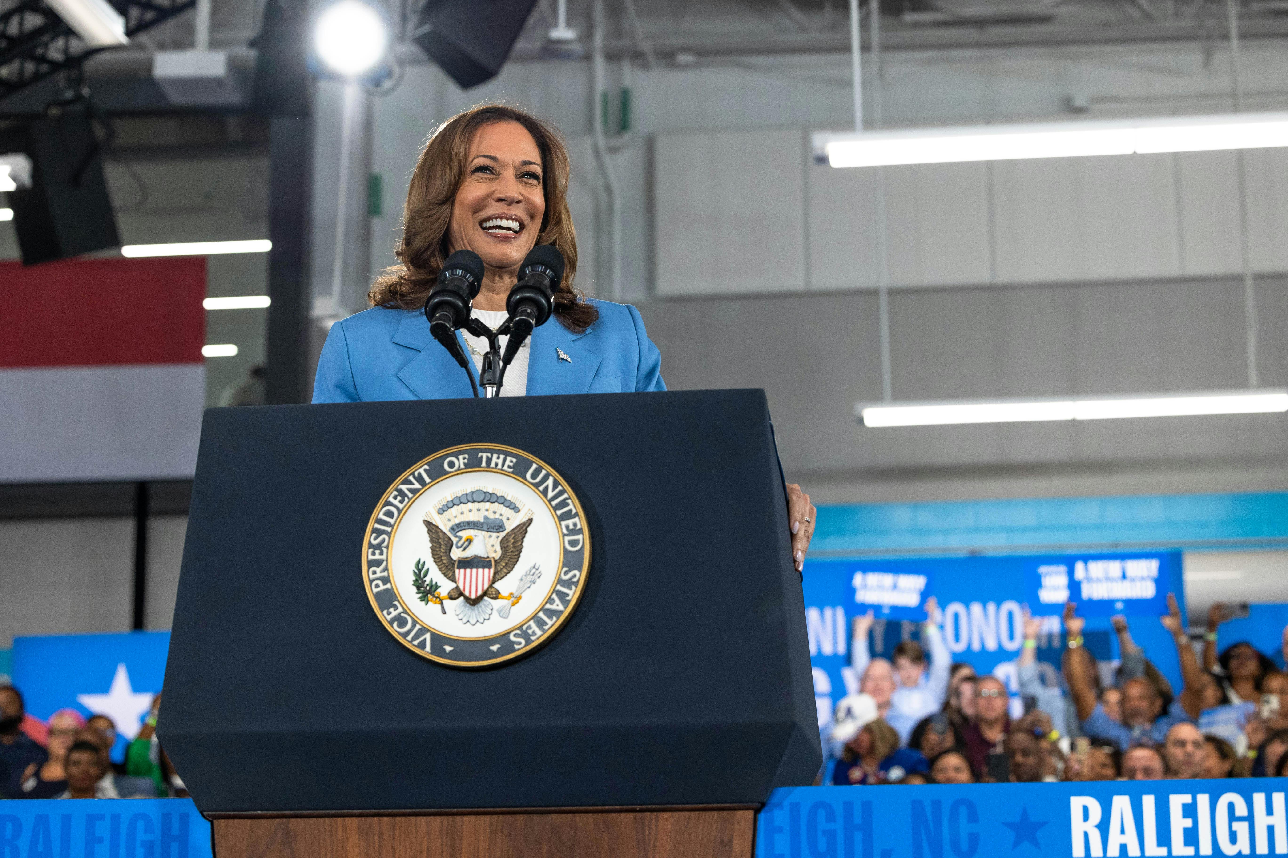 Kamala Harris smiles at a podium with audience members behind her.