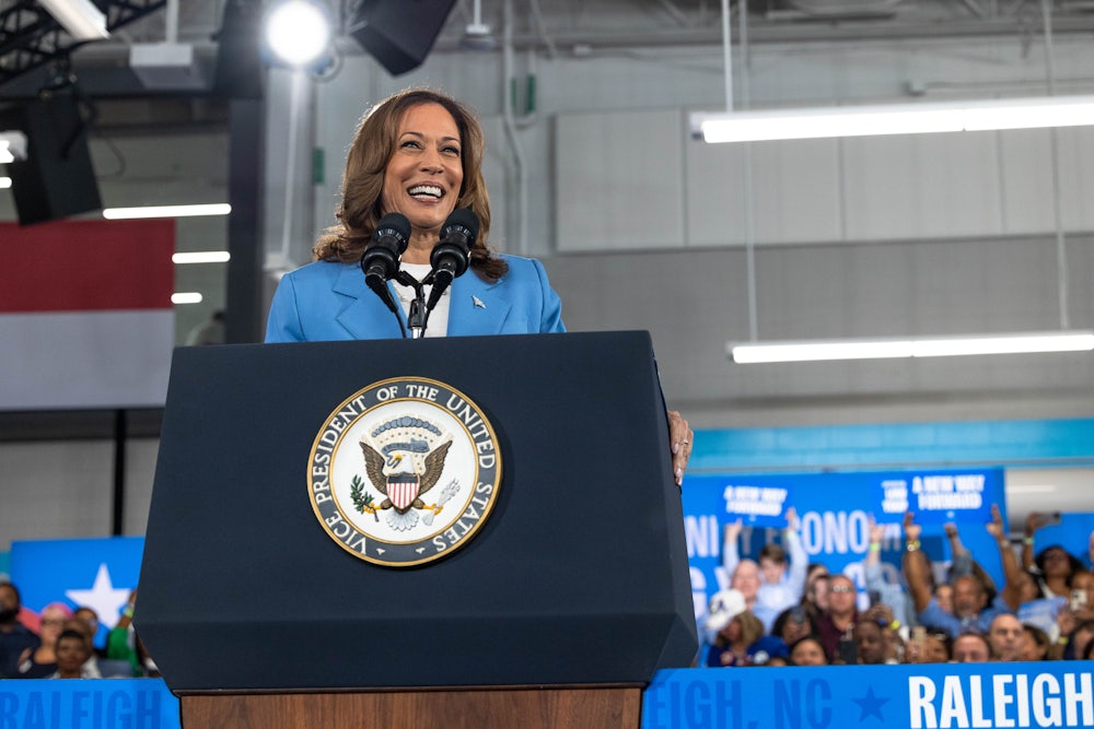 Kamala Harris smiles at a podium with audience members behind her.