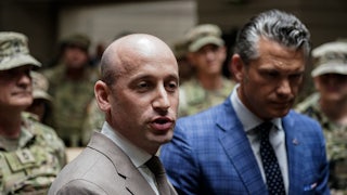 Stephen Miller speaks while standing next to Defense Secretary Pete Hegseth. They are surrounded by troops.