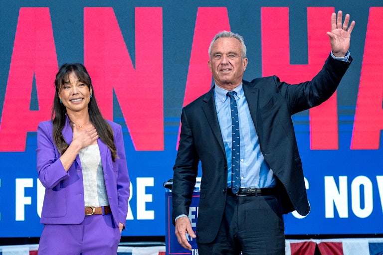 Nicole Shanahan puts an arm on her chest and Robert F. Kennedy Jr waves as they both stand on a stage during their campaign rally in 2024.