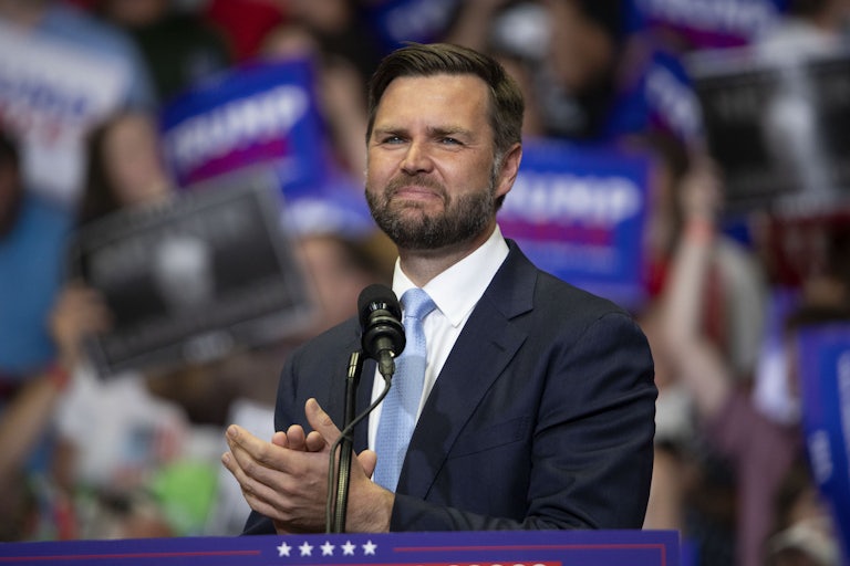J.D. Vance claps while standing at the podium during a joint rally with Donald Trump