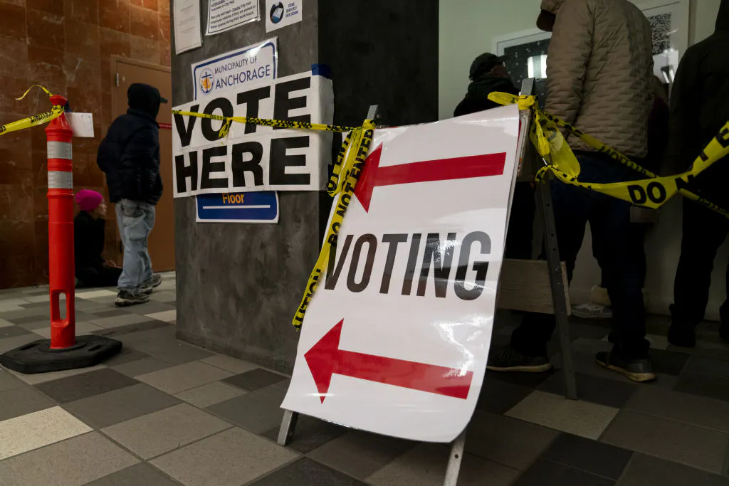 People stand in line to vote. Voting signs and Do Not Enter tape are hung up.