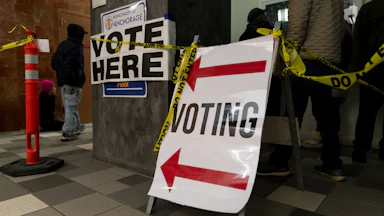 People stand in line to vote. Voting signs and Do Not Enter tape are hung up.