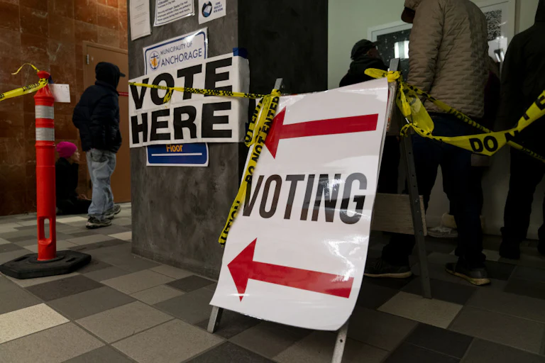 People stand in line to vote. Voting signs and Do Not Enter tape are hung up.