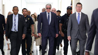 Leon Black walks in a group of people while wearing sunglasses inside