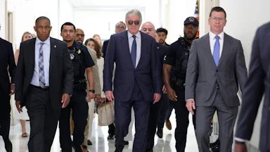 Leon Black walks in a group of people while wearing sunglasses inside
