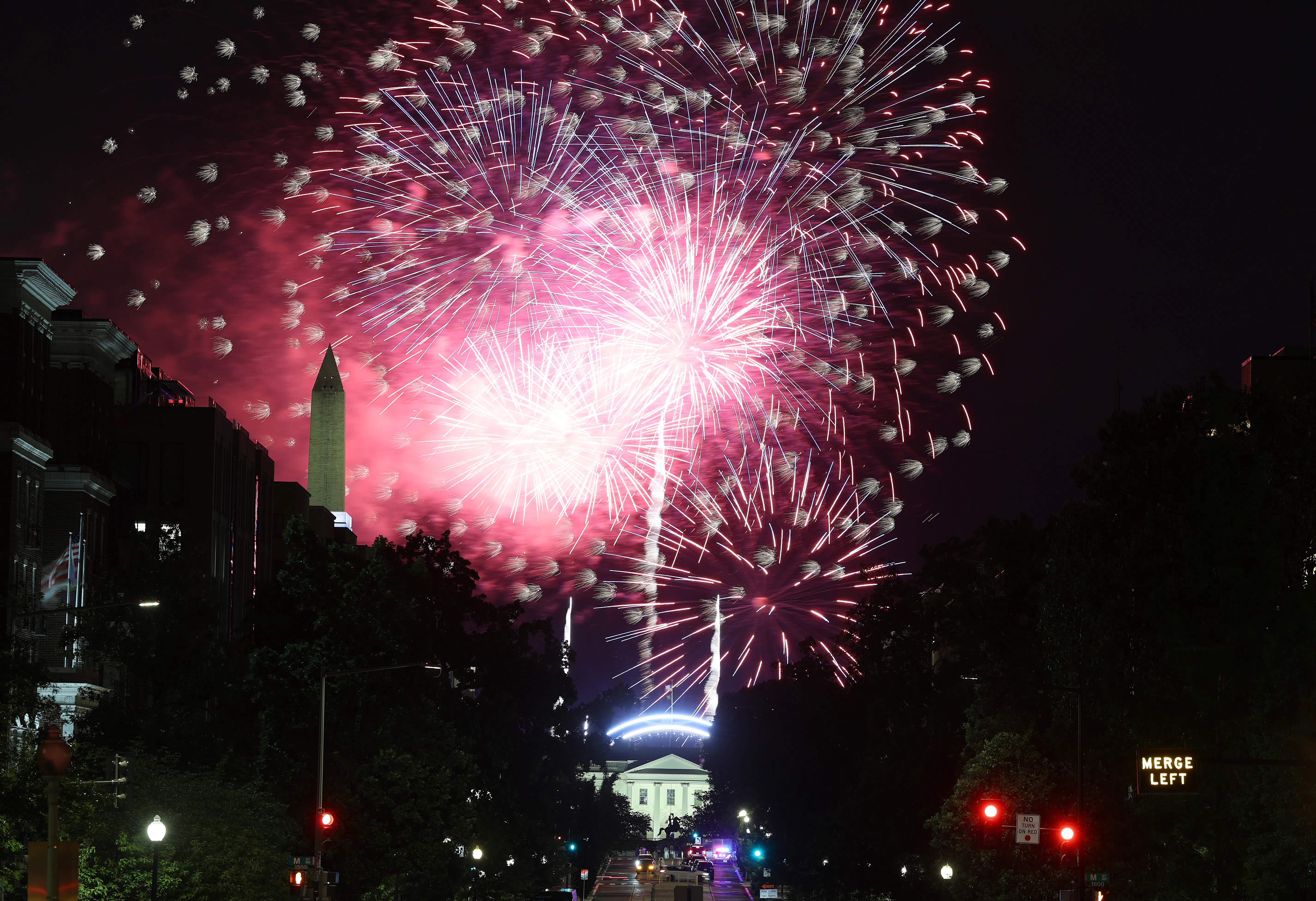Fireworks are visible in the sky above Washington, D.C., with the Washington Monument and White House visible in the background.