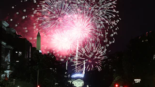 Fireworks are visible in the sky above Washington, D.C., with the Washington Monument and White House visible in the background.