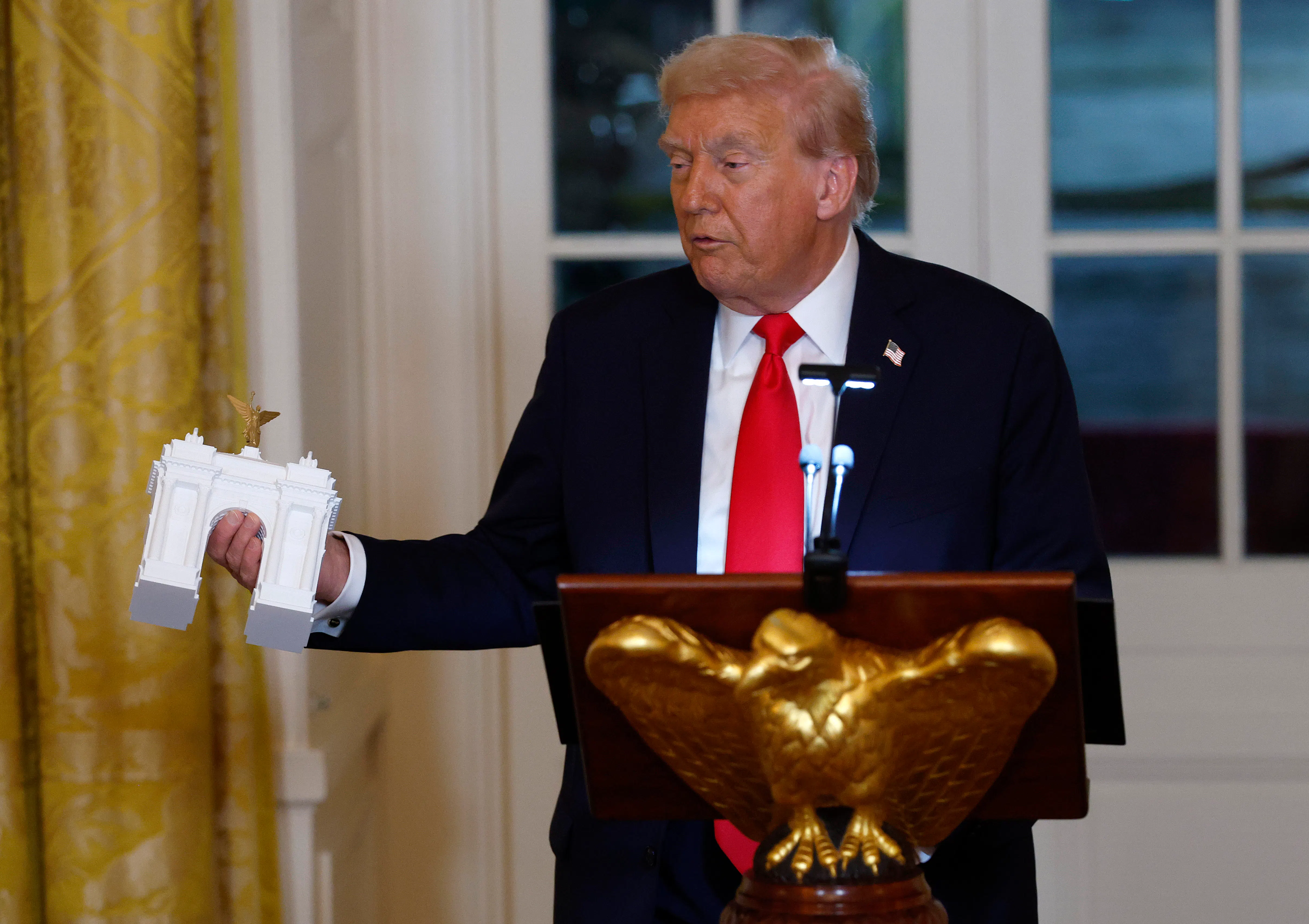 Donald Trump holds a model of an arch as he delivers remarks during a ballroom fundraising dinner in the East Room.