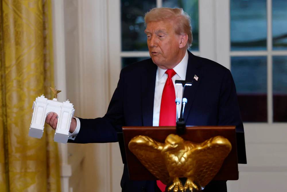Donald Trump holds a model of an arch as he delivers remarks during a ballroom fundraising dinner in the East Room.