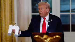 Donald Trump holds a model of an arch as he delivers remarks during a ballroom fundraising dinner in the East Room.