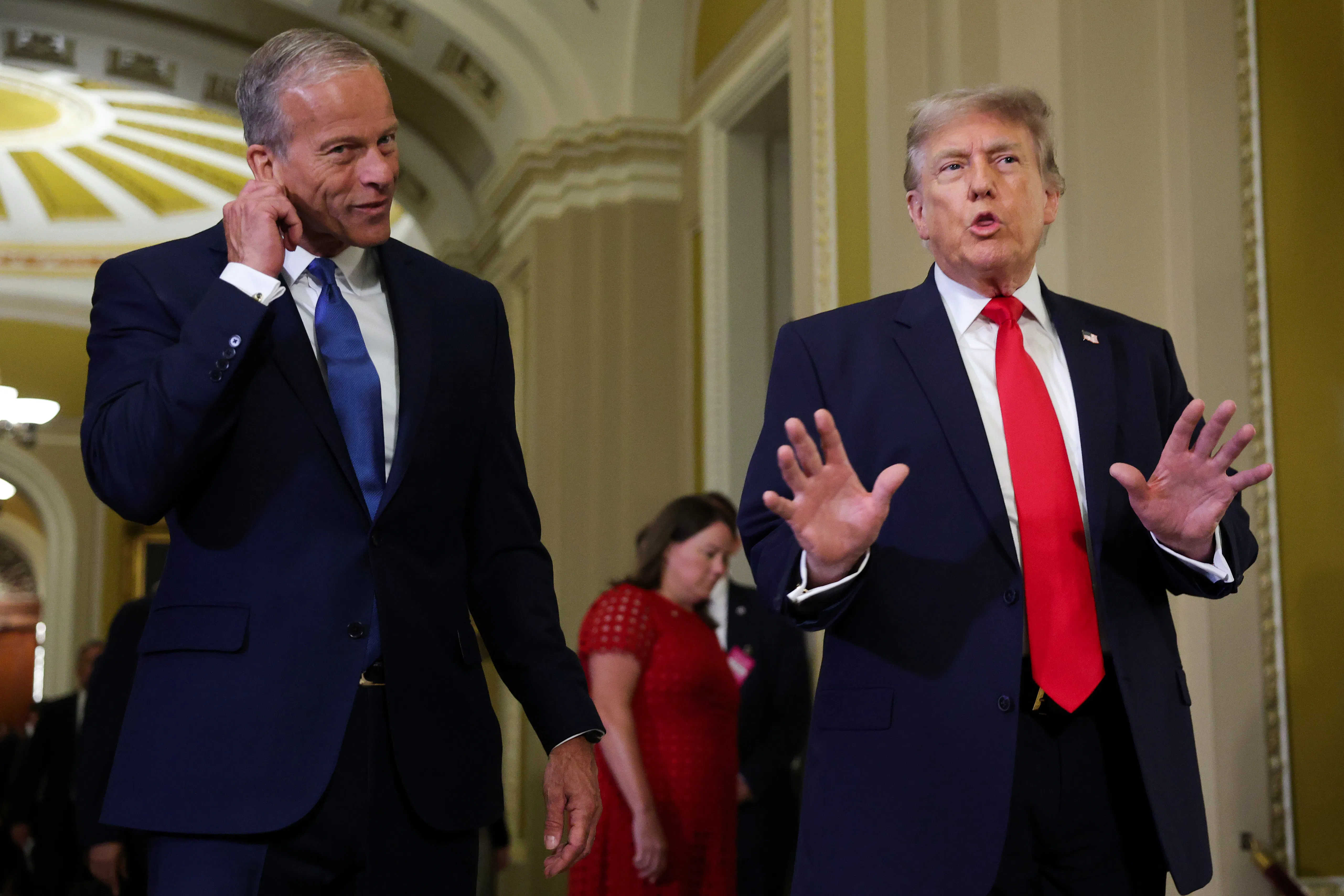 John Thune, left, in a navy suit and dark tie, holds his ear while Donald Trump speaks while wearing a blue suit and red tie. 