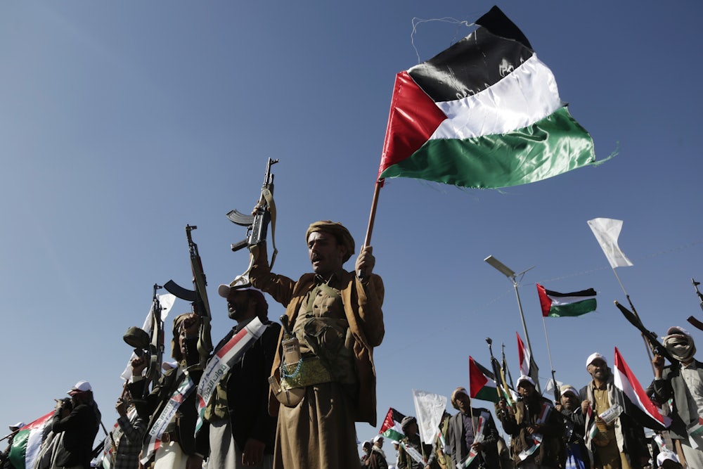 Yemenis recently trained by the Houthi movement hold up their guns and a Palestinian flag during an armed popular parade held in Al-Sabeen Square to get ready to go and fight Israel in the Gaza Strip, on December 02, 2023 in Sana'a, Yemen.