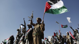 Yemenis recently trained by the Houthi movement hold up their guns and a Palestinian flag during an armed popular parade held in Al-Sabeen Square to get ready to go and fight Israel in the Gaza Strip, on December 02, 2023 in Sana'a, Yemen.