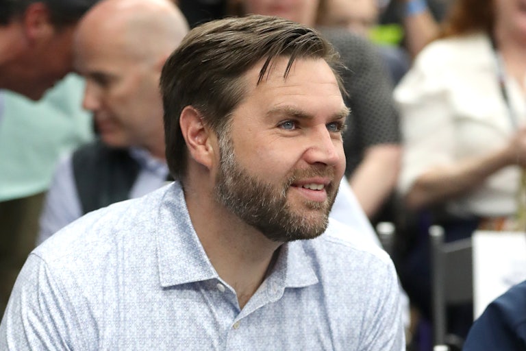 JD Vance smiles while wearing a gray polo as he leans forward in a crowd