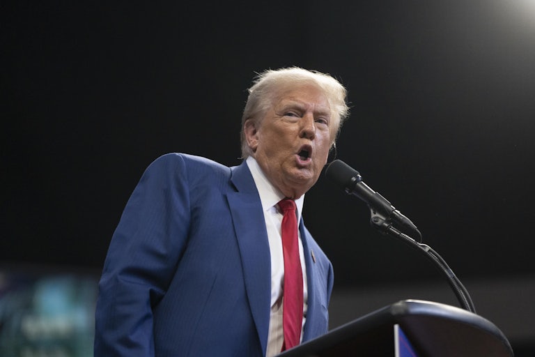 Donald Trump leans over and speaks into a microphone