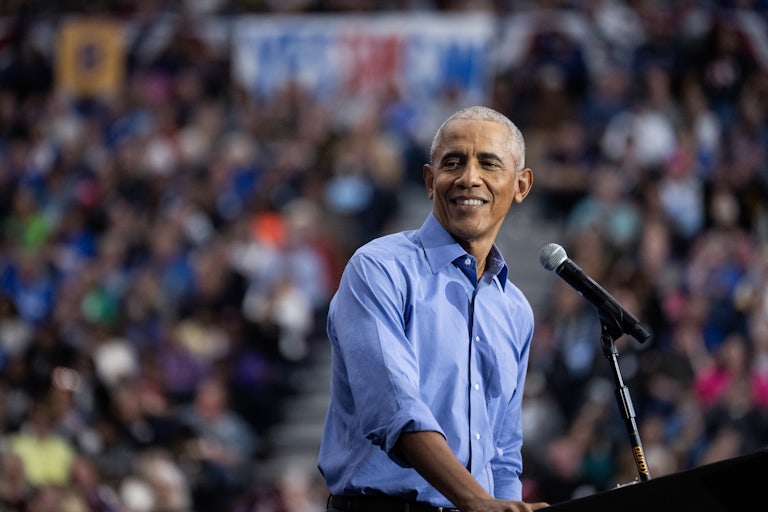 Barack Obama smiles and looks to the side while standing at a podium during a Kamala Harris event