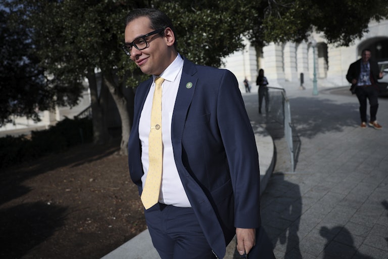 Representative George Santos smiles and walks, briefcase in hand.