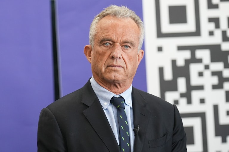 RFK Jr. seated, stares off into space. Part of a QR code is behind him.