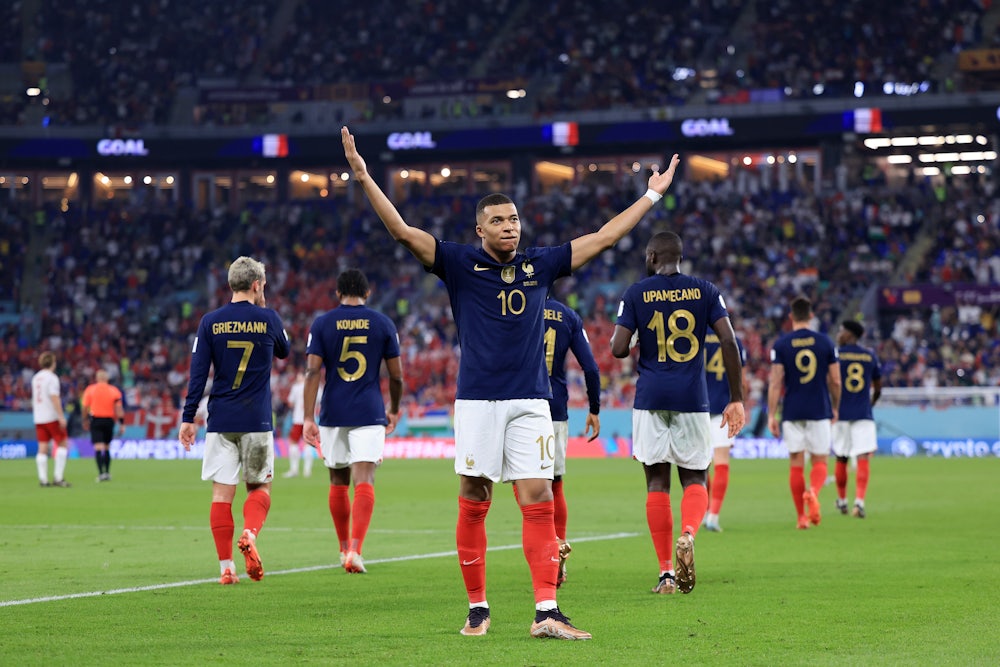 French striker Kylian Mbappe holds his arms aloft after scoring a goal as his teammates walk back to their half.