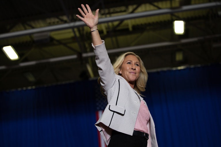 Representative Marjorie Taylor Greene on stage waves her hand to a crowd not pictured