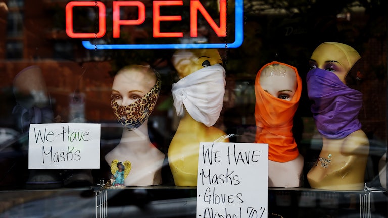 Mannequin heads wear masks in the window of a small boutique