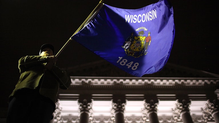 A man waves the Wisconsin state flag on the steps of the state capitol in Madison.