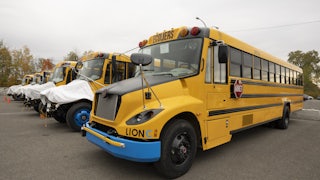 Row of 6 yellow electric school buses in a parking lot
