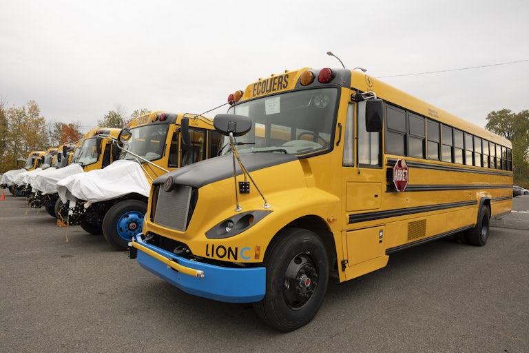Row of 6 yellow electric school buses in a parking lot