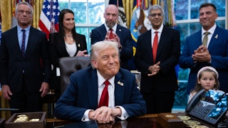 Donald Trump sits at his desk in the Oval Office of the White House, as RFK Jr. and others stand behind him.