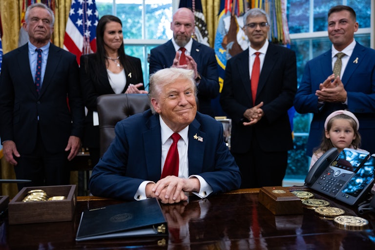 Donald Trump sits at his desk in the Oval Office of the White House, as RFK Jr. and others stand behind him.