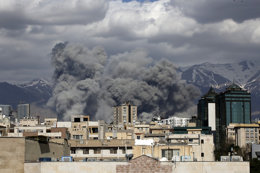 Smoke rises above buildings, with mountains in the background.