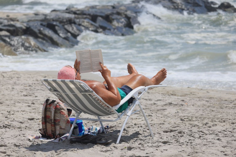 A person relaxes on a beach with a book.