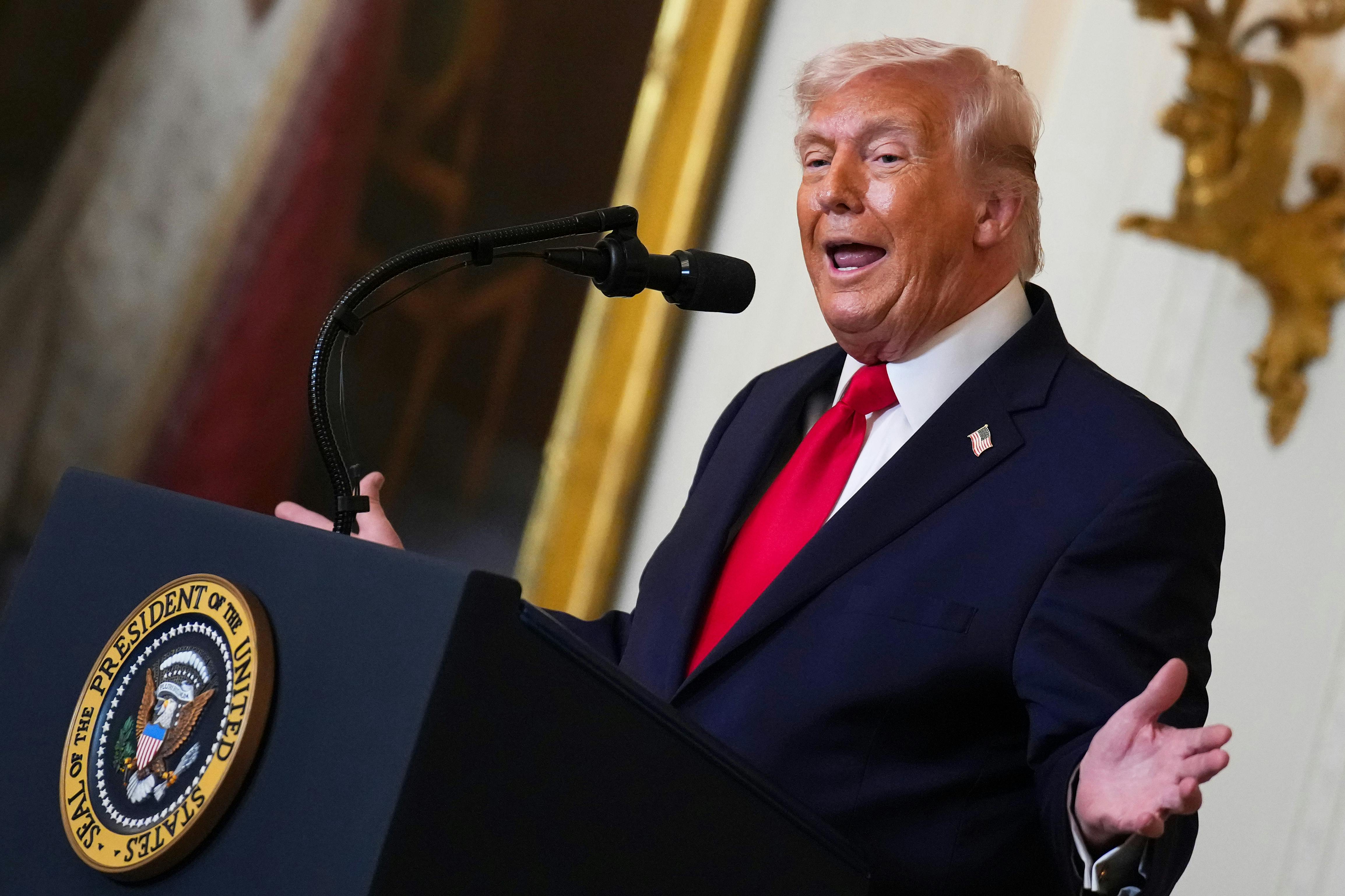 Donald Trump gestures with both hands while speaking at a podium