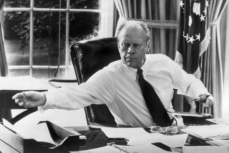 President Gerald Ford reaches across his desk in the Oval Office.