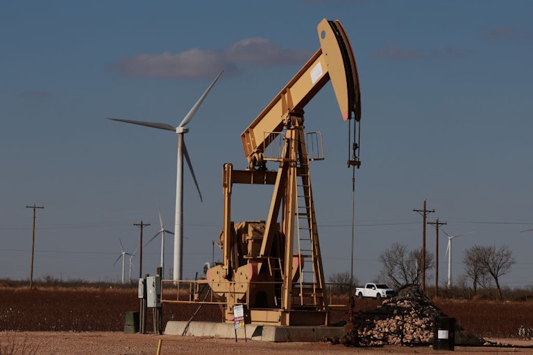 An oil pump jack with wind turbines in the background