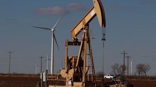 An oil pump jack with wind turbines in the background