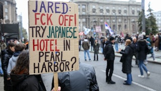 A protester in Serbia holds a sign that reads, "Jared: Fck Off! Try Japanese hotel in Pear Harbor?"