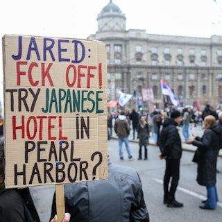 A protester in Serbia holds a sign that reads, "Jared: Fck Off! Try Japanese hotel in Pear Harbor?"