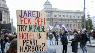 A protester in Serbia holds a sign that reads, "Jared: Fck Off! Try Japanese hotel in Pear Harbor?"