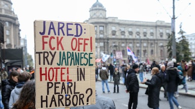 A protester in Serbia holds a sign that reads, "Jared: Fck Off! Try Japanese hotel in Pear Harbor?"