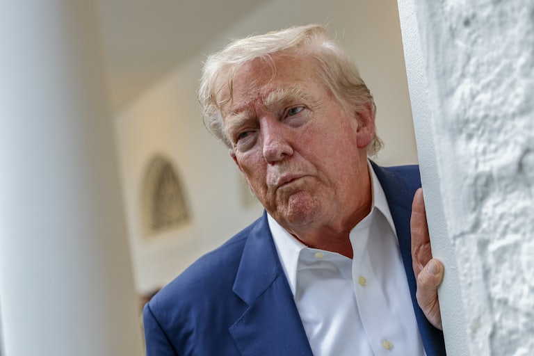 Donald Trump purses his lips while leaning against an outdoor wall at the White House