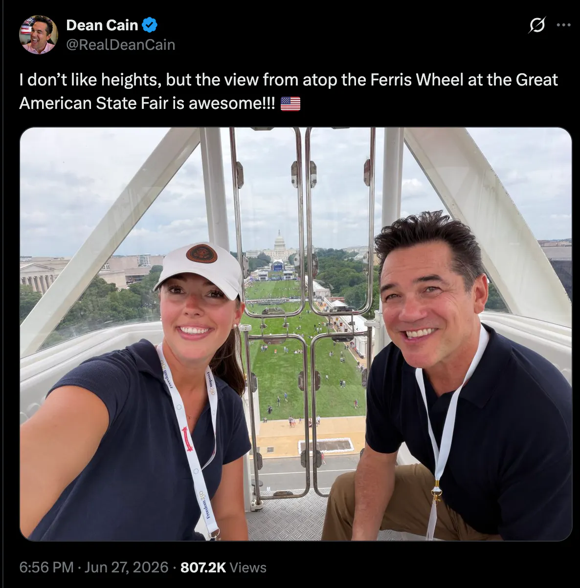 A screenshot of an X post from Dean Cain reading "I don’t like heights, but the view from atop the Ferris Wheel at the Great American State Fair is awesome!!! 🇺🇸" A photo is included of him sitting at a large height overlooking the National Mall with sparse crowds below. 