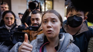 Greta Thunberg holds up a finger while speaking, surrounded by others.