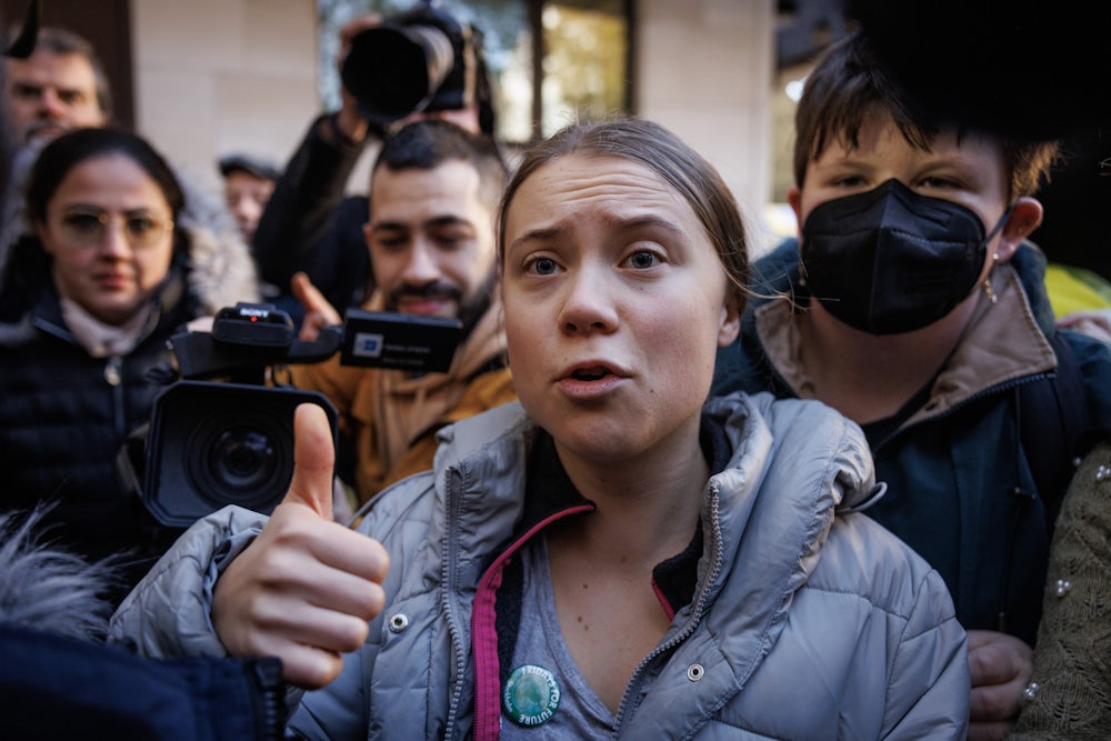 Greta Thunberg holds up a finger while speaking, surrounded by others.