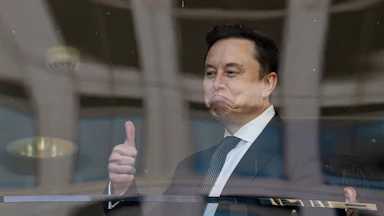 Elon musk frowns and gives a thumbs up