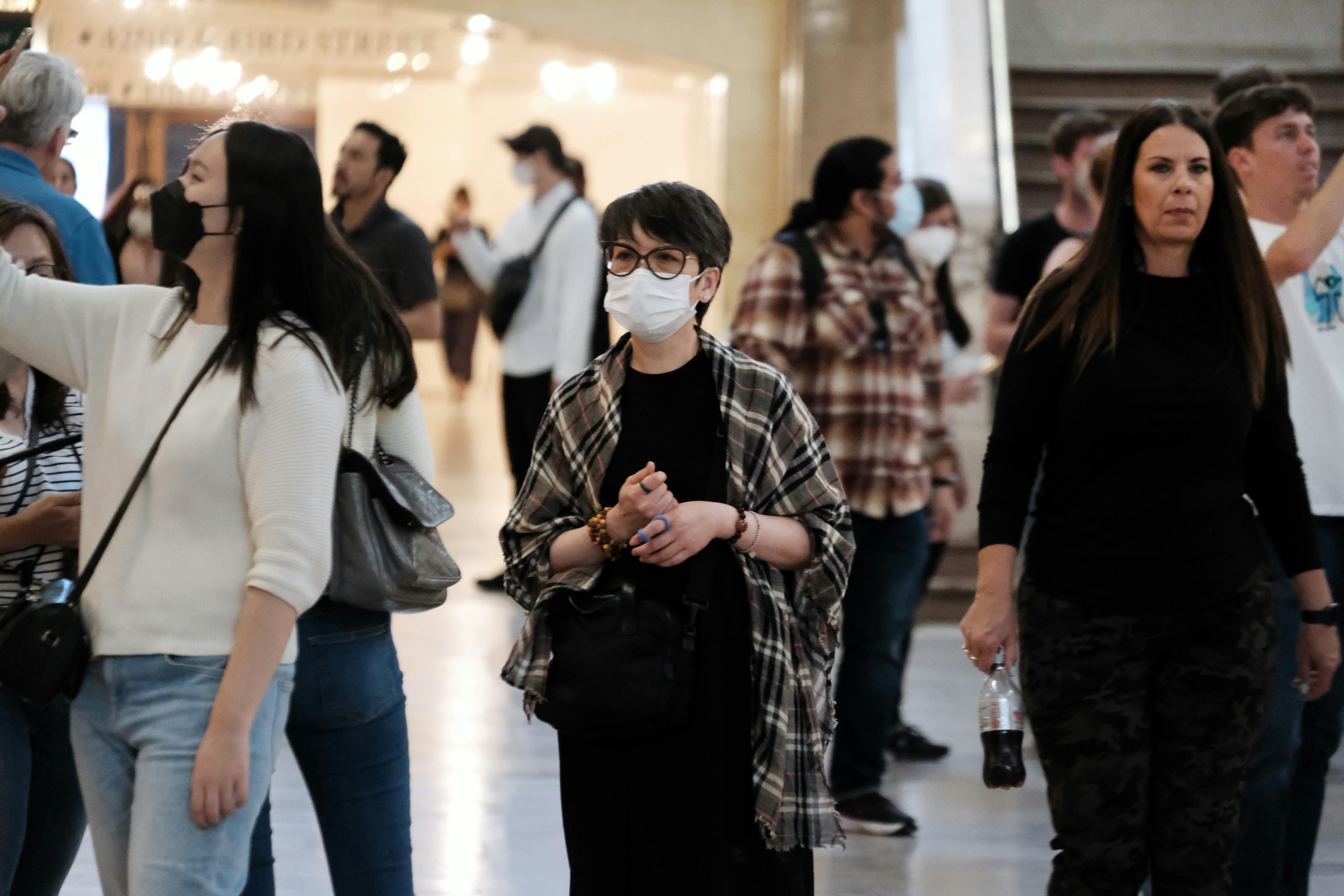 A woman wears a mask, surrounded by others maskless.