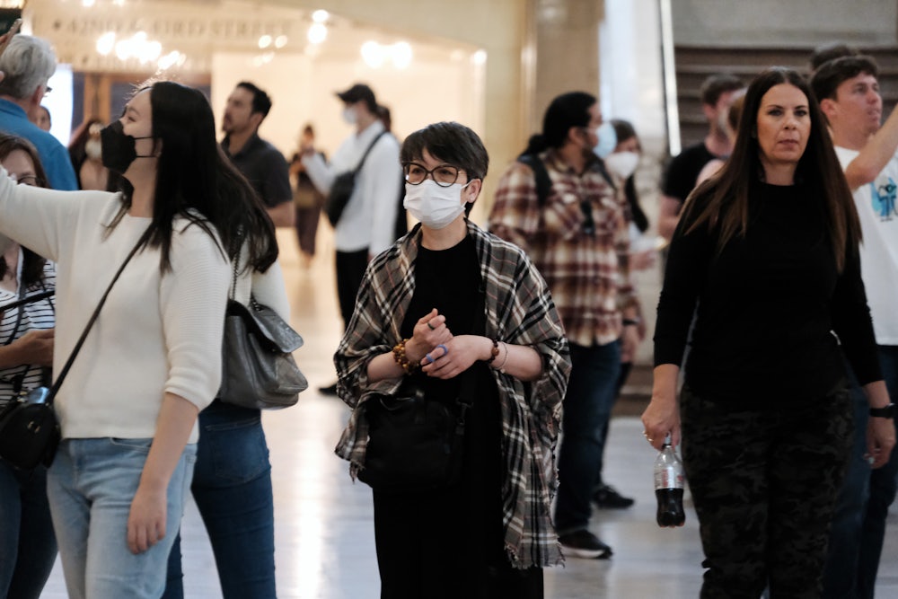 A woman wears a mask, surrounded by others maskless.