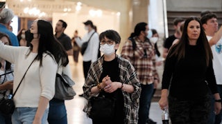 A woman wears a mask, surrounded by others maskless.