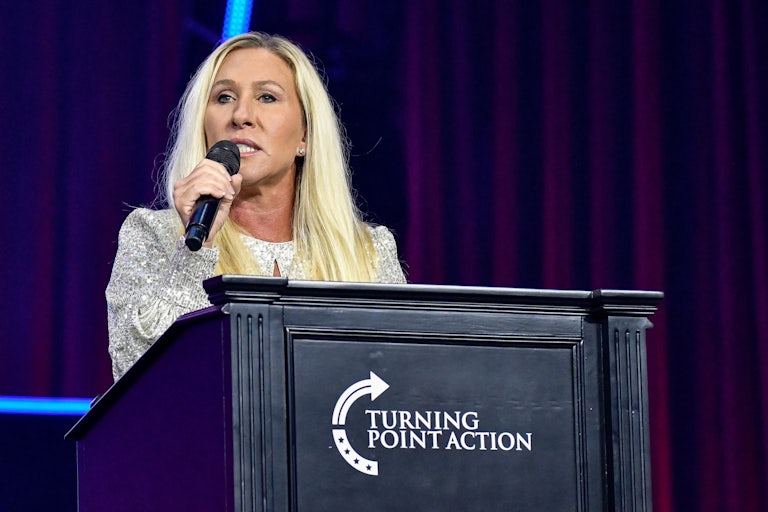 Marjorie Taylor Greene speaks into a microphone while standing at a podium